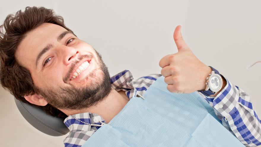 Junger Mann mit Bart zeit Daumen hoch auf dem Zahnarztstuhl in der Zahnarztpraxis