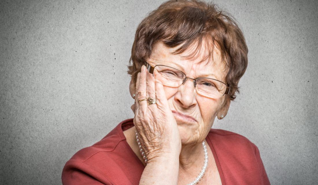 Seniorin hält sich die Wange, weil ihr Zahnersatz Beschwerden verursacht.